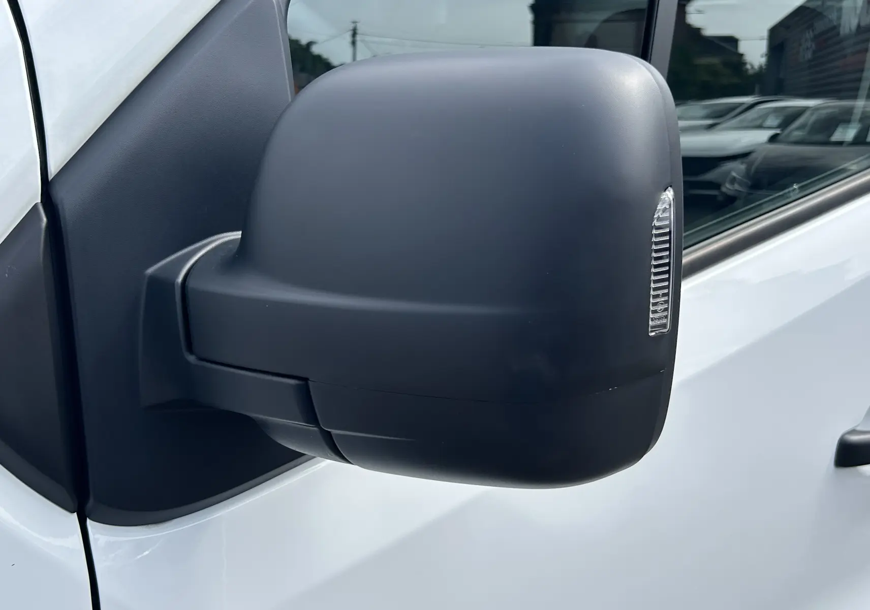 Gros plan sur le rétroviseur noir côté gauche du Renault Trafic Fourgon blanc, avec clignotant intégré.
