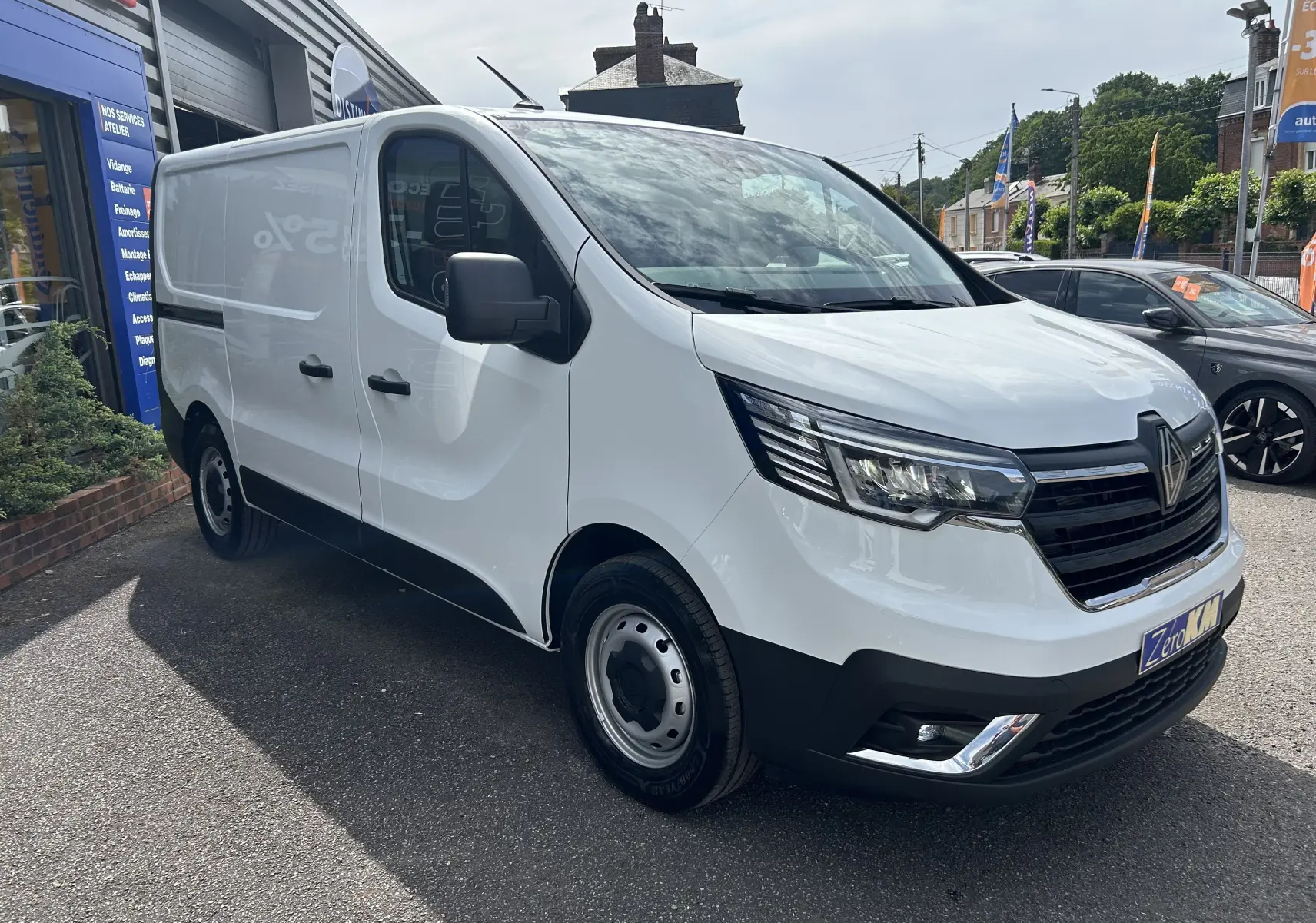 Renault Trafic Fourgon blanc vu en 3/4 avant droit, avec calandre noire et projecteurs modernes allumés.