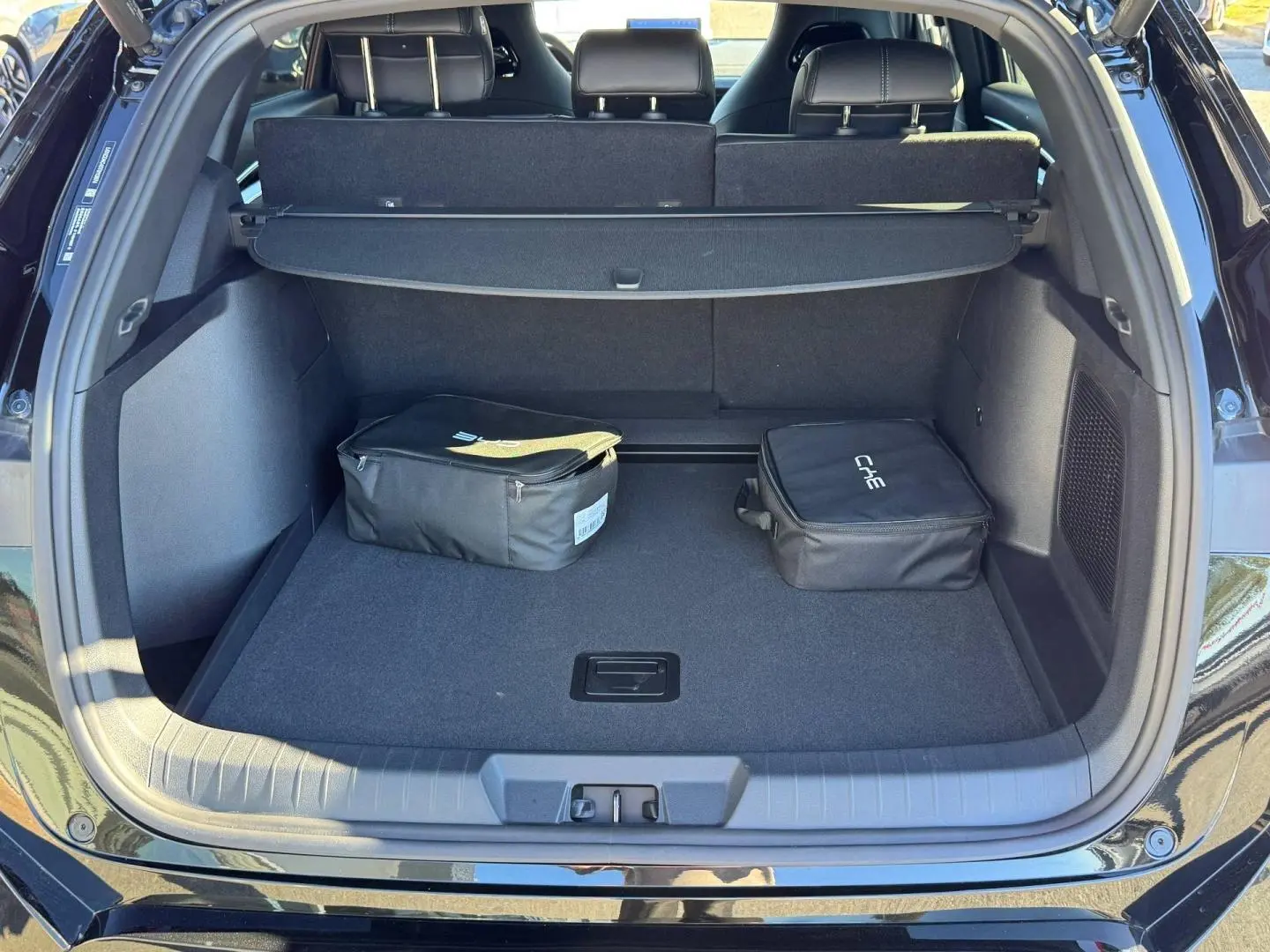 Coffre ouvert vu de l'arrière du BYD SEAL U noir métallisé avec cache-bagages et deux sacs noirs à l'intérieur.