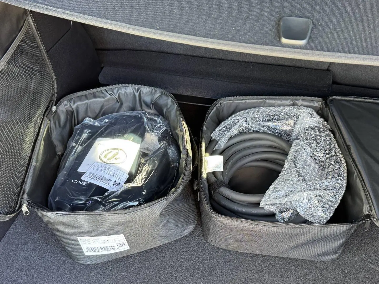 Vue du coffre du BYD SEAL U 2026 avec deux sacs noirs contenant des câbles de recharge.