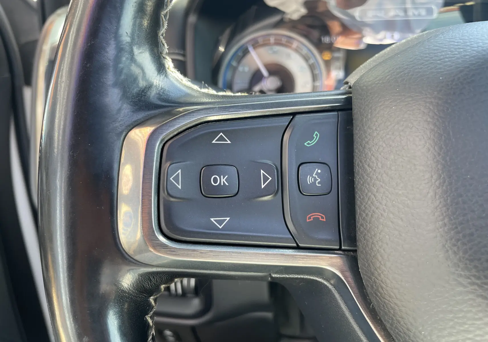 Gros plan sur les commandes au volant gauche du Dodge RAM 1500 blanc nacré, avec boutons de navigation et téléphone.