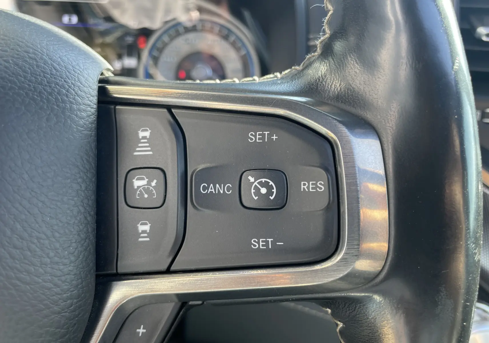 Gros plan sur les commandes de régulateur de vitesse au volant cuir noir du Dodge RAM 1500 blanc nacré.