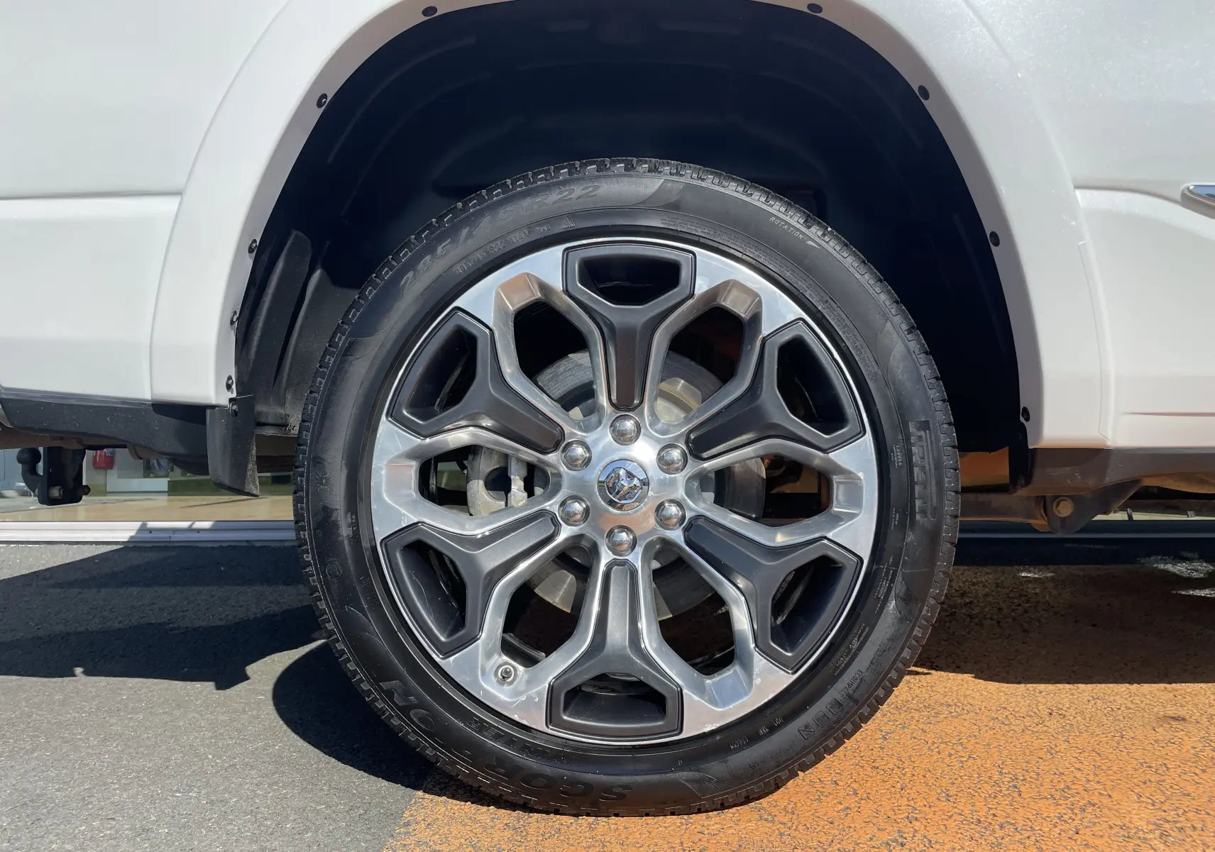 Gros plan sur la roue avant droite du Dodge RAM 1500 blanc nacré, mettant en valeur la jante alu au design moderne.