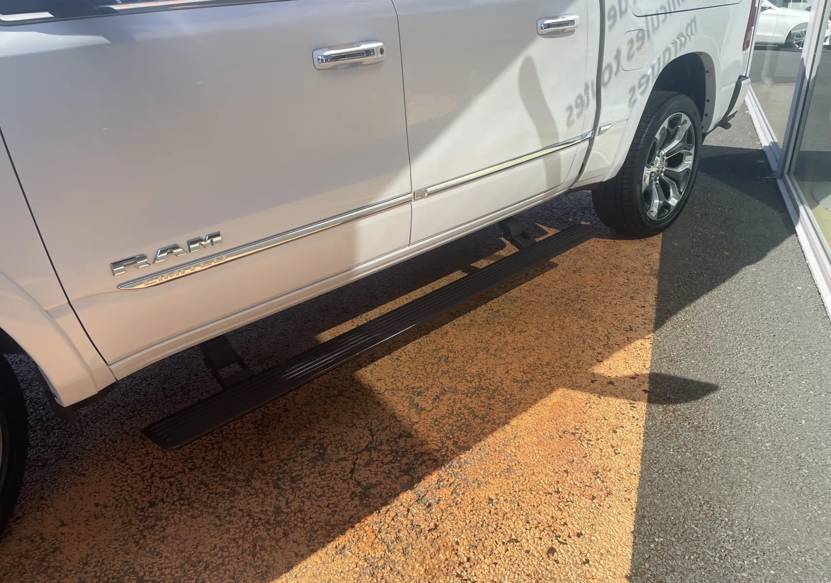 Vue latérale côté droit du Dodge RAM 1500 blanc nacré avec marchepied électrique et jantes chromées visibles.