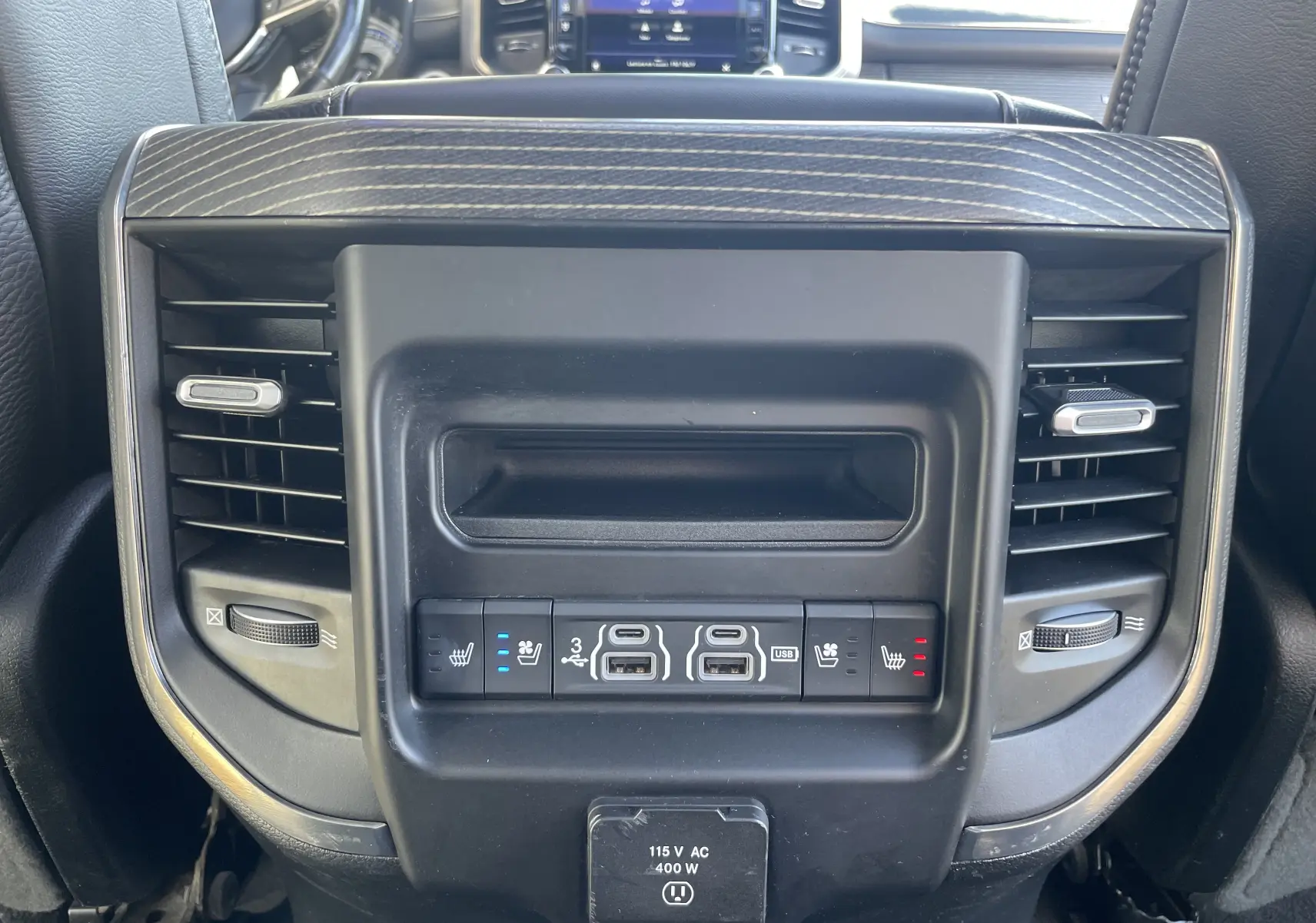 Gros plan sur la console arrière noire du Dodge RAM 1500 2020, avec commandes de sièges chauffants et ventilés, prises USB et prises d'air.