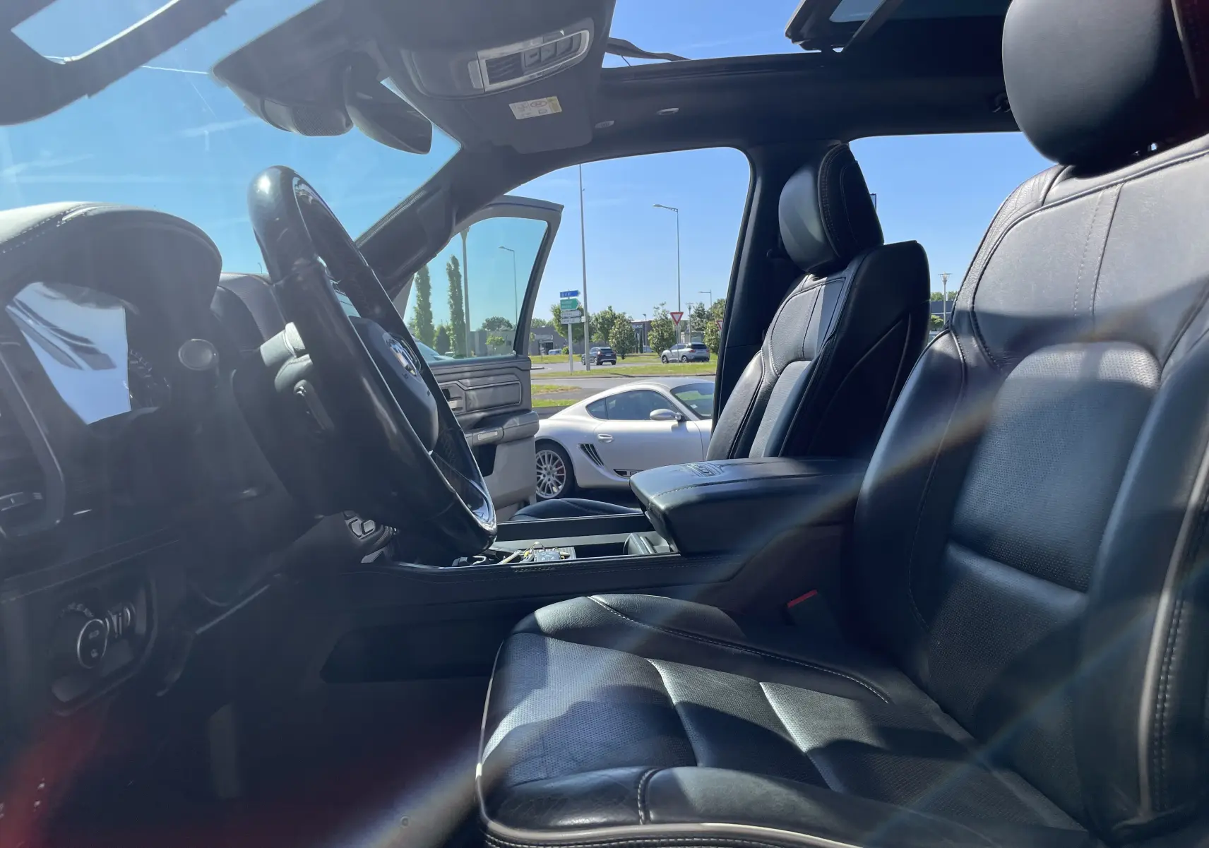 Vue intérieure côté conducteur du Dodge RAM 1500 blanc nacré, sièges cuir noir et toit ouvrant panoramique visibles.
