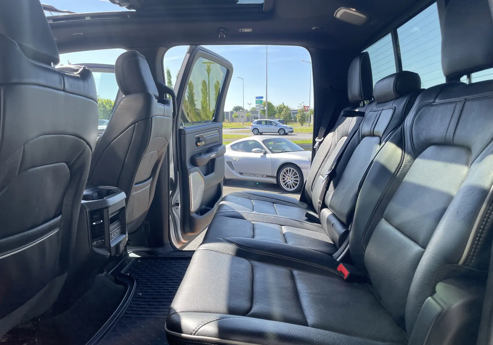 Intérieur arrière du Dodge RAM 1500 blanc nacré, sièges cuir noir et porte arrière gauche ouverte sur parking.