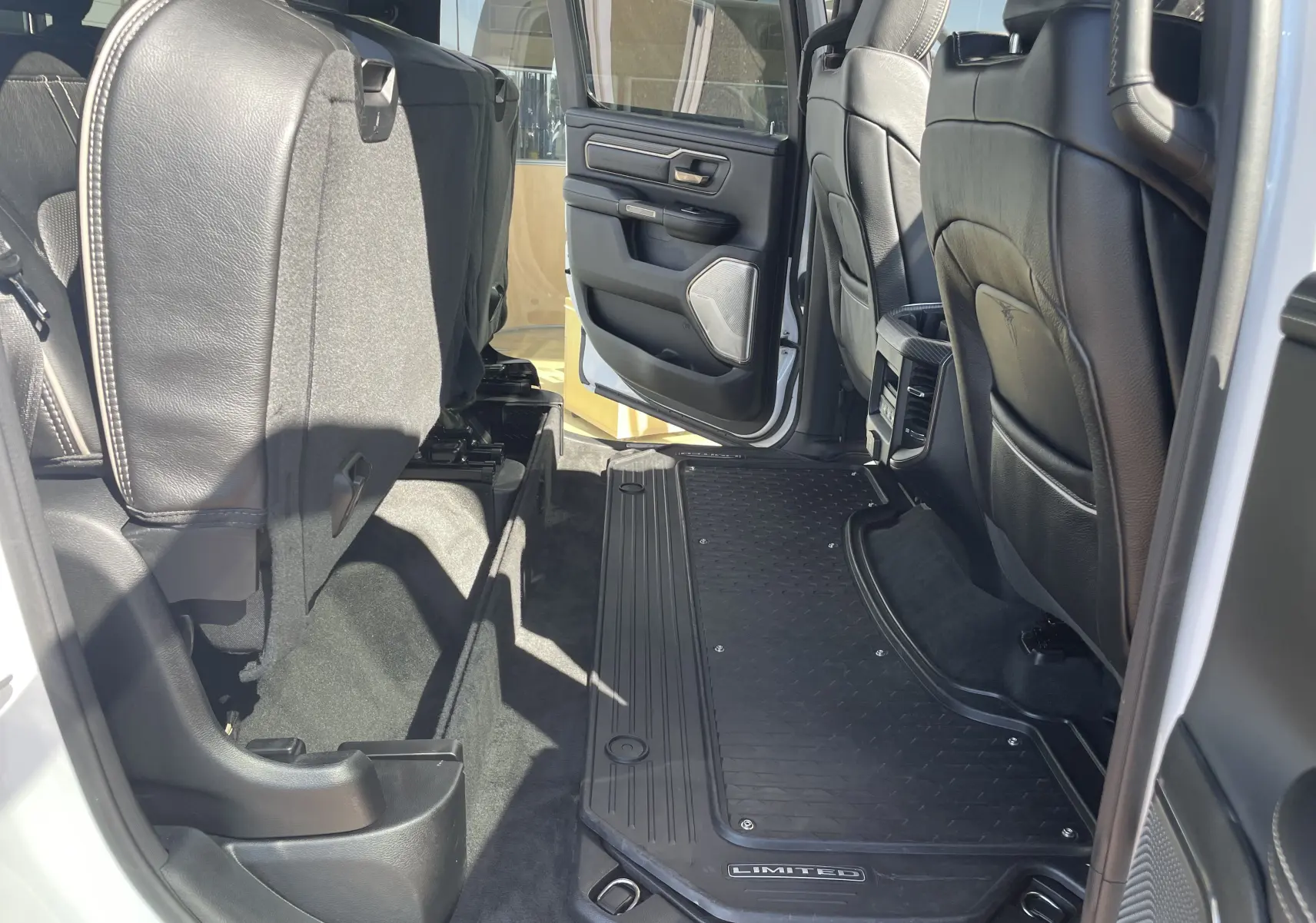 Vue intérieure côté droit arrière du Dodge RAM 1500 blanc nacré, mettant en valeur les sièges cuir noir et tapis Limited.