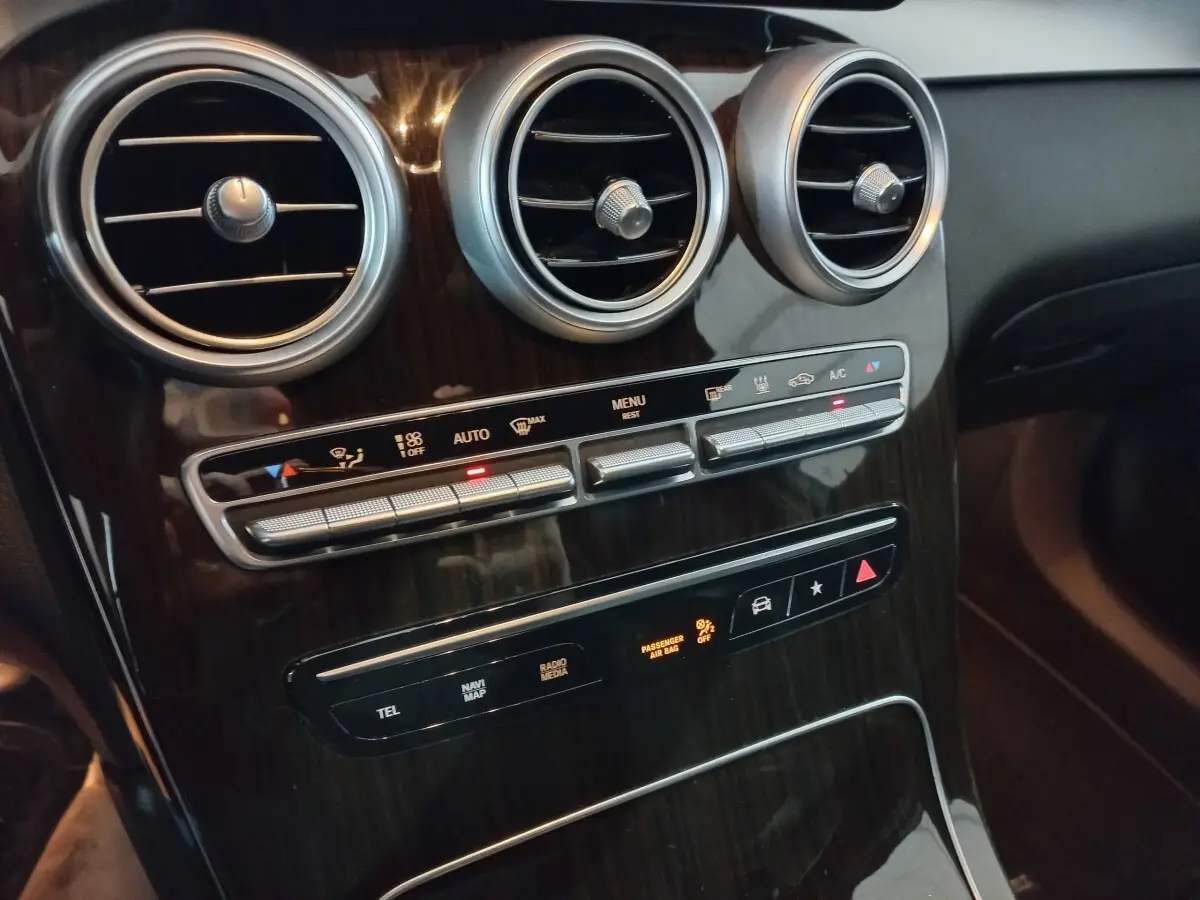 Vue rapprochée du tableau de bord noir brillant avec aérateurs ronds et commandes climatisation du Mercedes GLC 300 E Business Line.