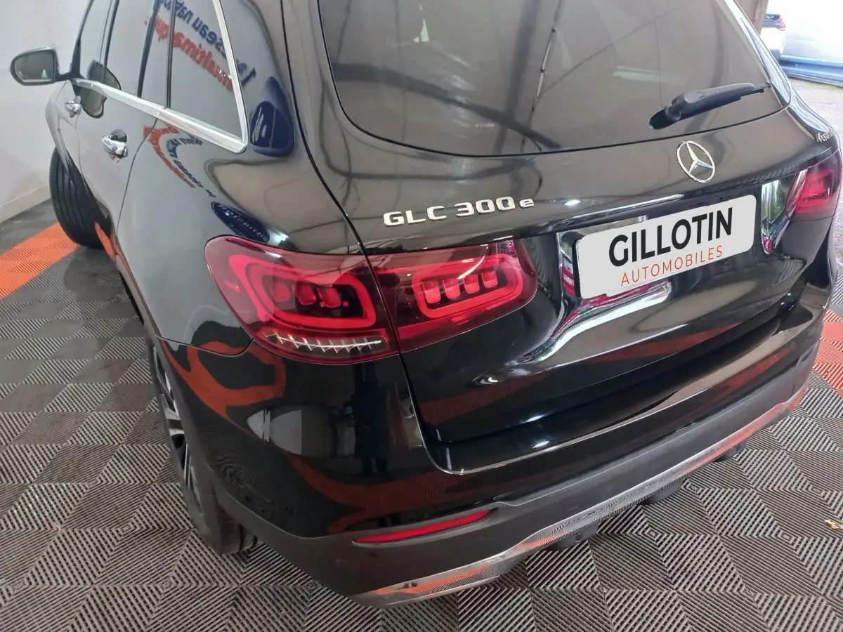 Vue 3/4 arrière gauche d'un Mercedes GLC 300e noir brillant avec feux arrière LED et logo sur coffre.