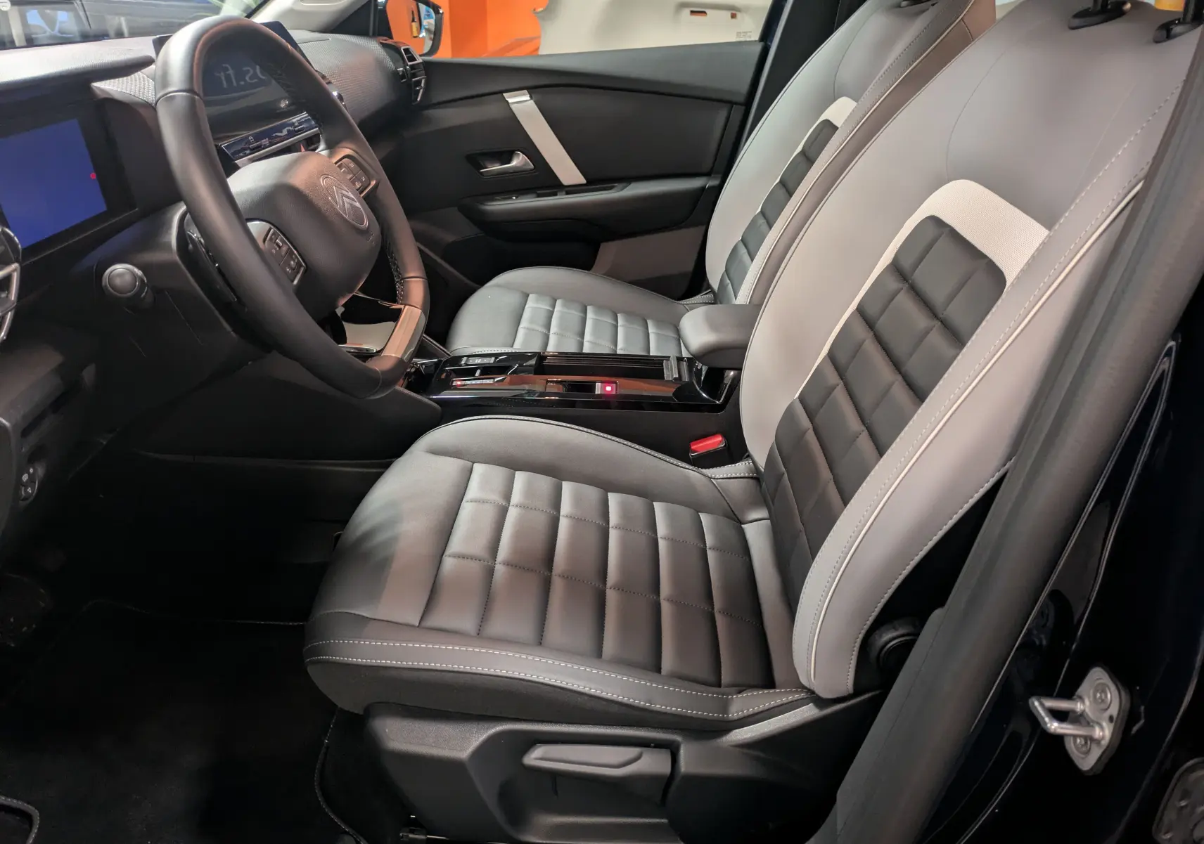 Vue intérieure côté conducteur de la Citroën C4 Hybride 2025 avec sièges bi-ton gris et noir et volant multifonction.