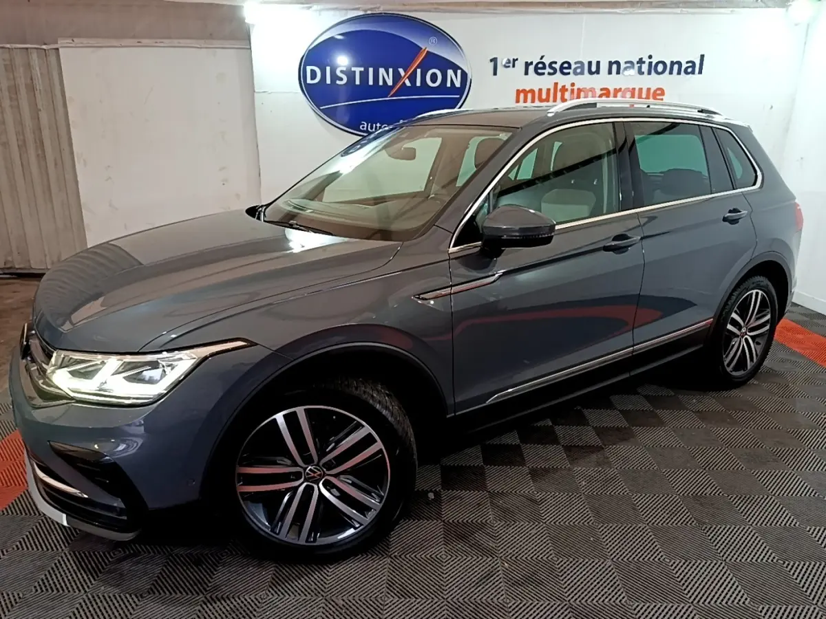 Volkswagen Tiguan gris clair vu en 3/4 avant droit, avec phares LED allumés et jantes alliage distinctives.