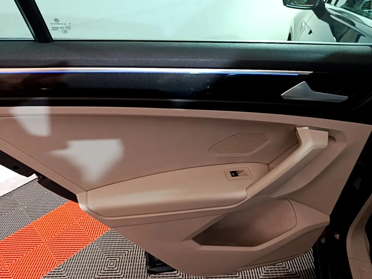Vue intérieure du panneau de porte côté gauche beige du Volkswagen Tiguan 2022 avec éclairage d'ambiance bleu fin.