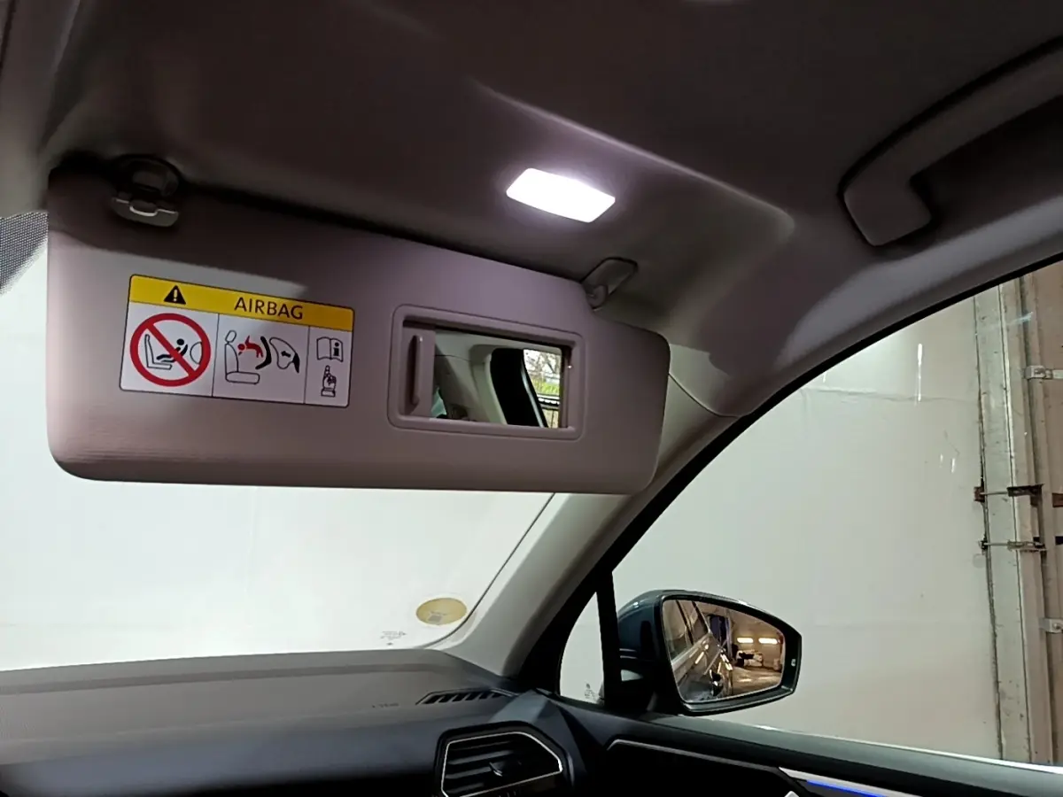 Vue intérieure côté conducteur du Volkswagen Tiguan gris clair 2022, avec pare-soleil baissé et miroir intégré allumé.