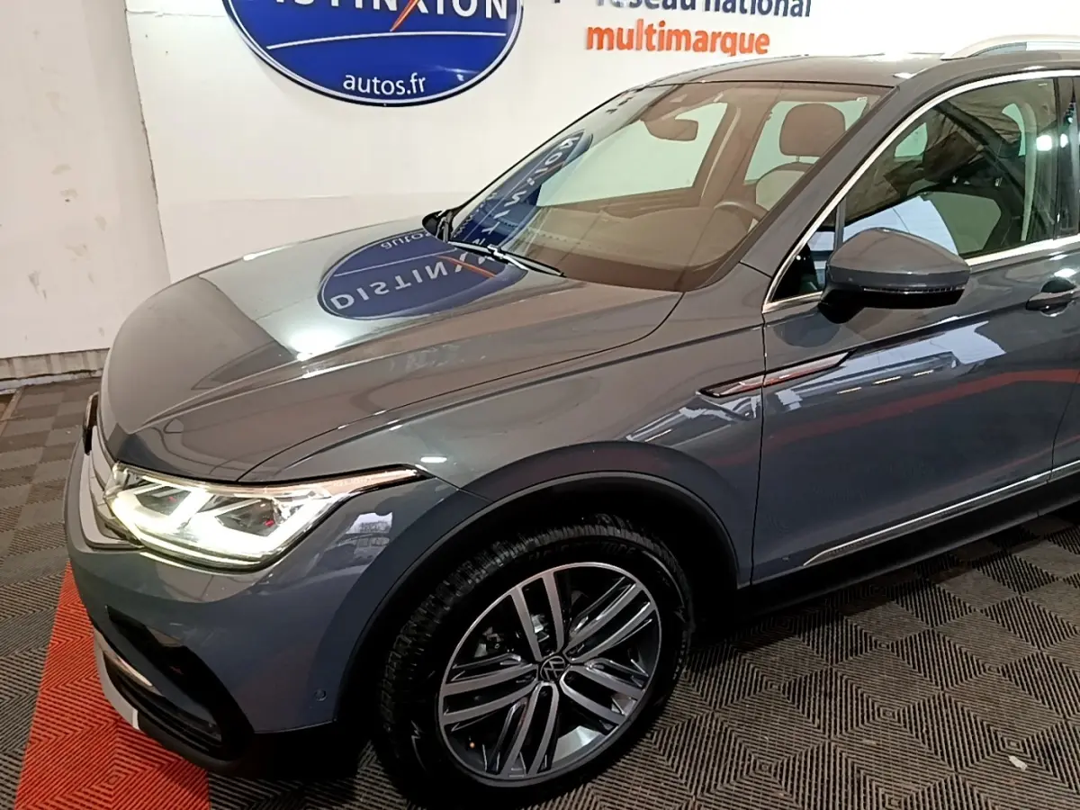 Vue 3/4 avant droit d'un Volkswagen Tiguan gris clair avec phares LED allumés et jantes alliage distinctives.