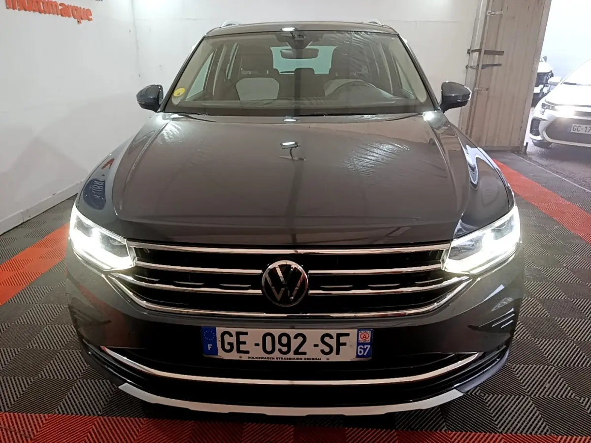 Vue avant d'un Volkswagen Tiguan gris clair avec phares LED allumés et calandre chromée brillante.