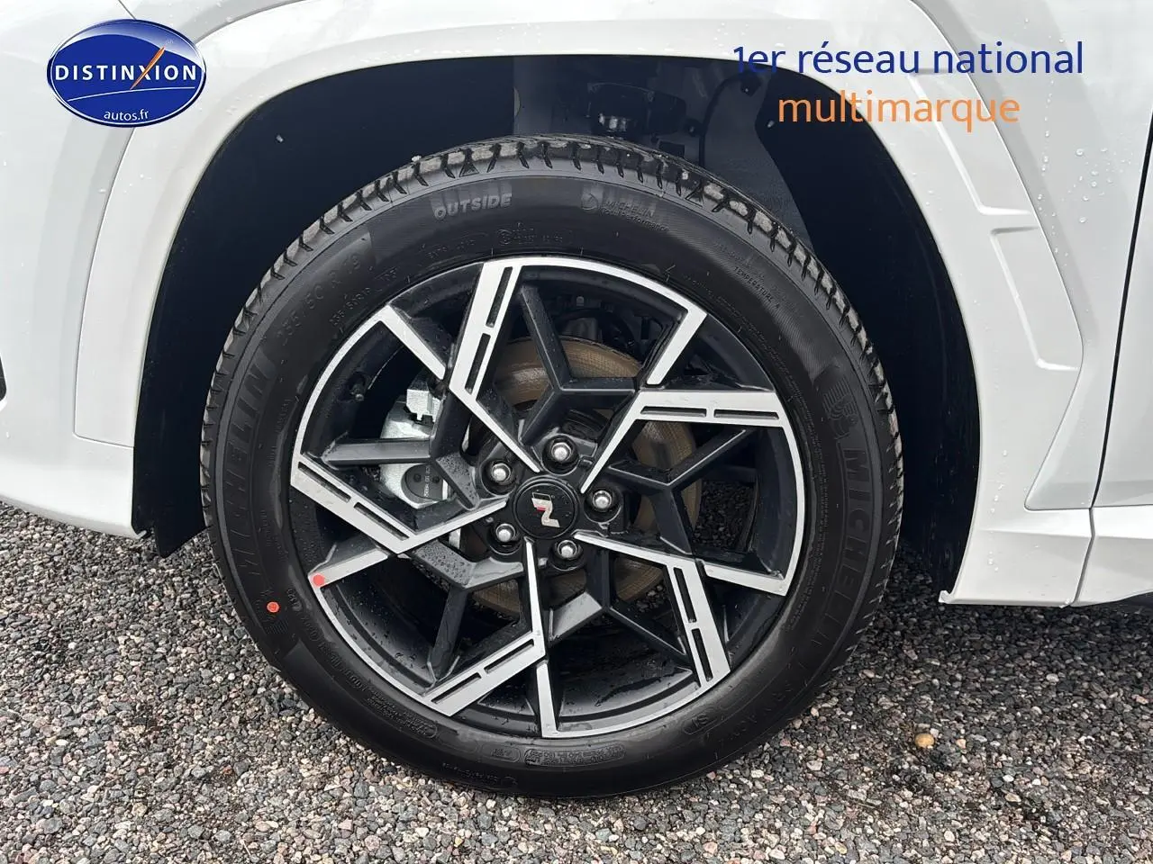 Gros plan sur la jante alliage 19 pouces noire et argent du côté gauche d’un Hyundai Tucson blanc sérénité.