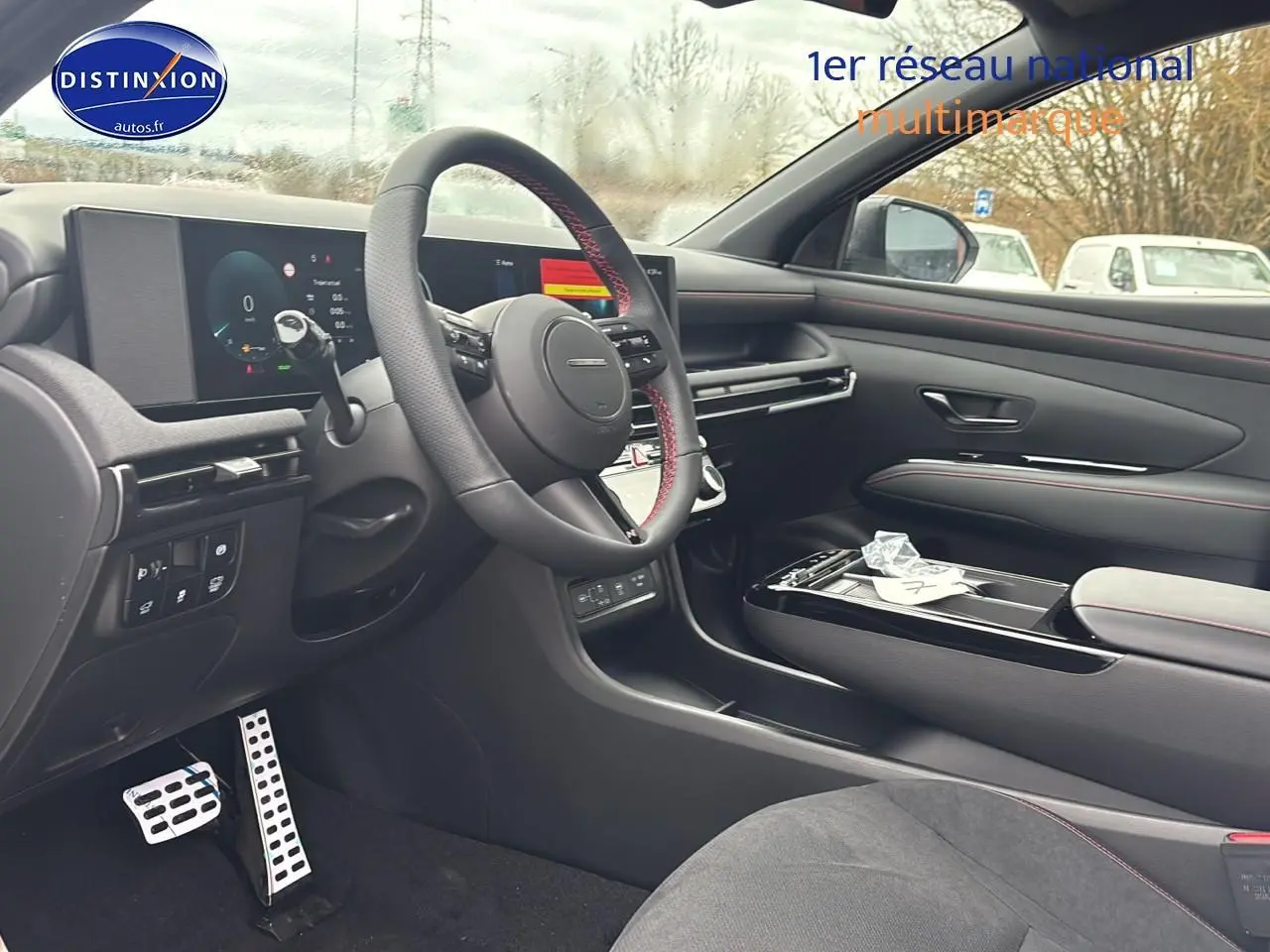 Vue intérieure côté conducteur du Hyundai Tucson 2026, volant cuir avec surpiqûres rouges et tableau de bord digital.