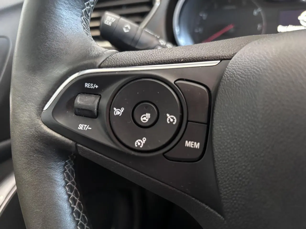 Gros plan sur les commandes de régulateur de vitesse au volant noir de l’Opel Grandland rouge foncé.