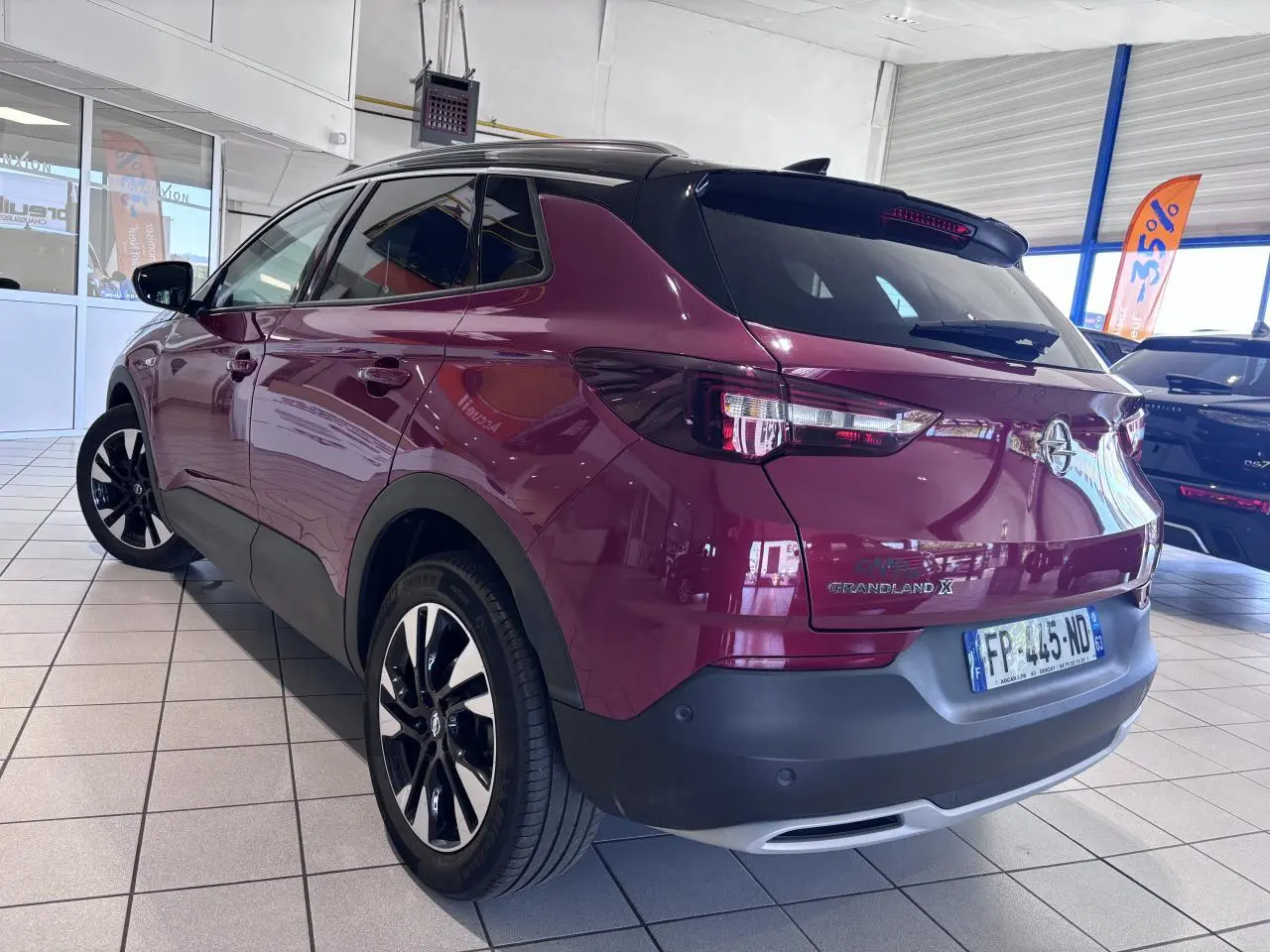 Vue 3/4 arrière droite d’un Opel Grandland X rouge foncé avec jantes alliage noires et toit noir en showroom.