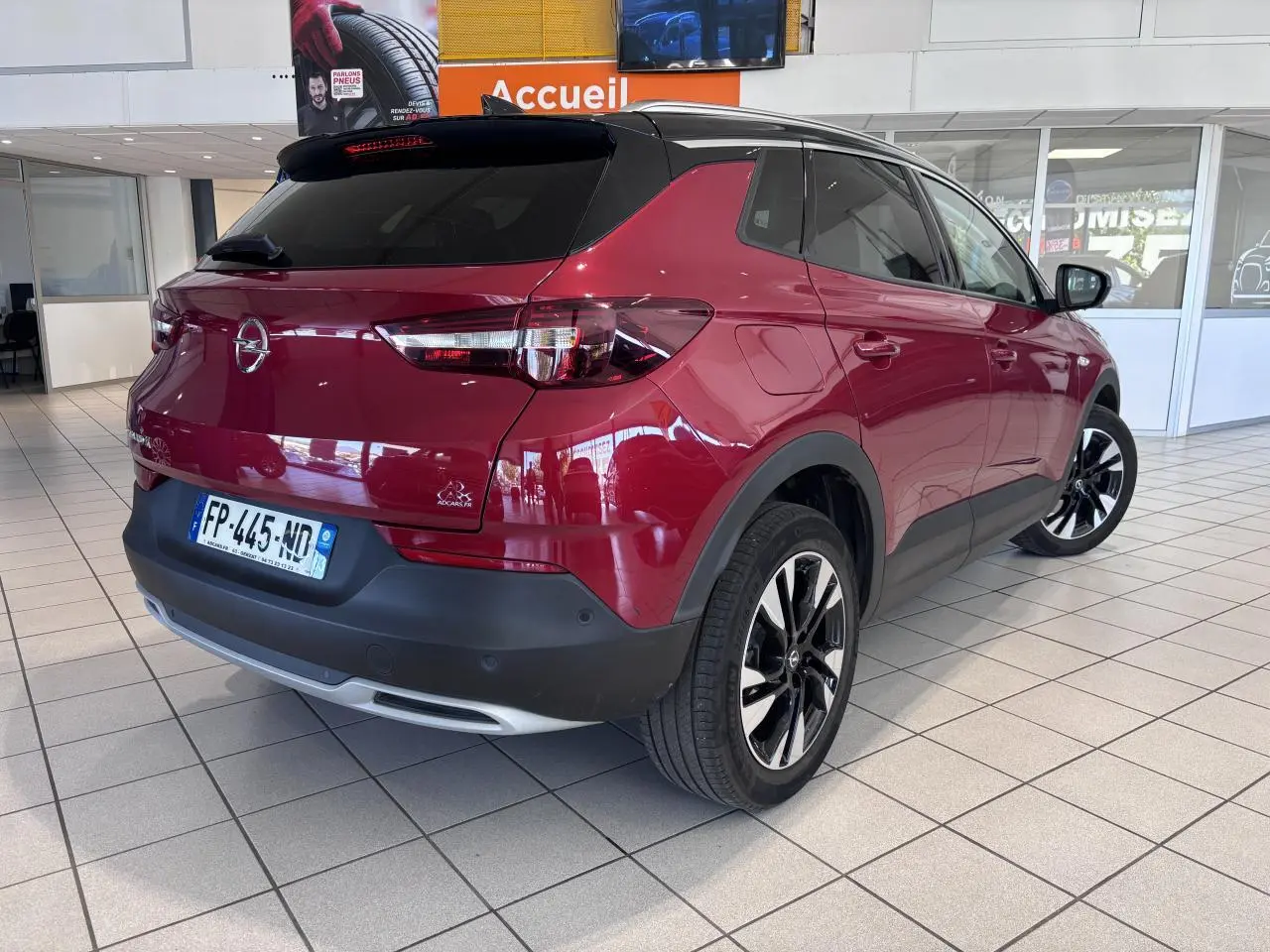 Vue 3/4 arrière droite d'un Opel Grandland rouge foncé avec toit noir et jantes alliage 19 pouces en showroom.
