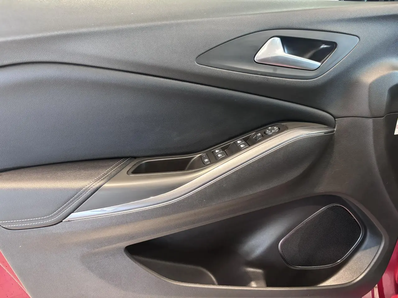 Vue rapprochée de la porte avant gauche noire avec commandes électriques et haut-parleur d’un Opel Grandland rouge foncé.