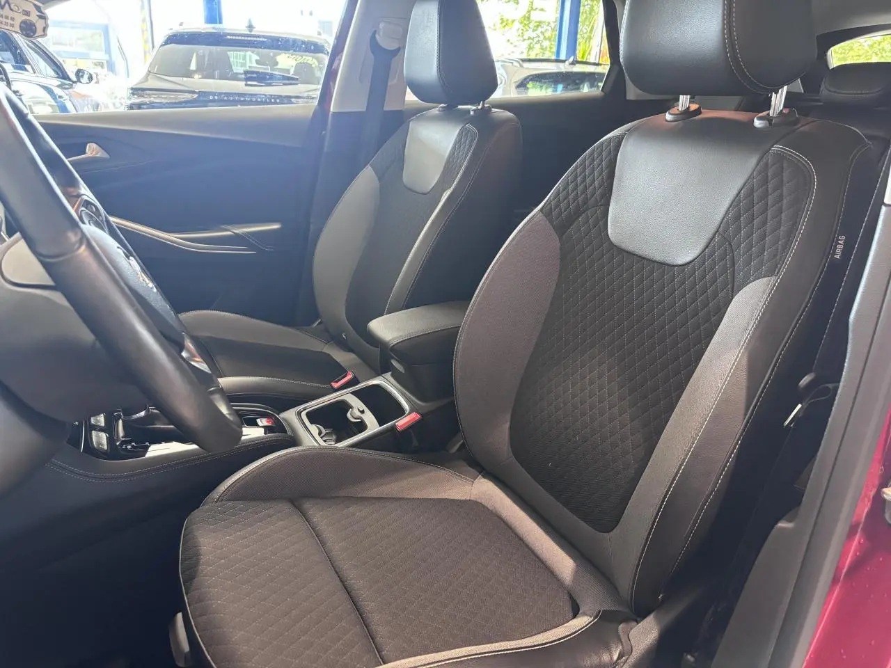 Vue intérieure côté avant droit de l'Opel Grandland rouge foncé, montrant les sièges avant en tissu noir et gris.