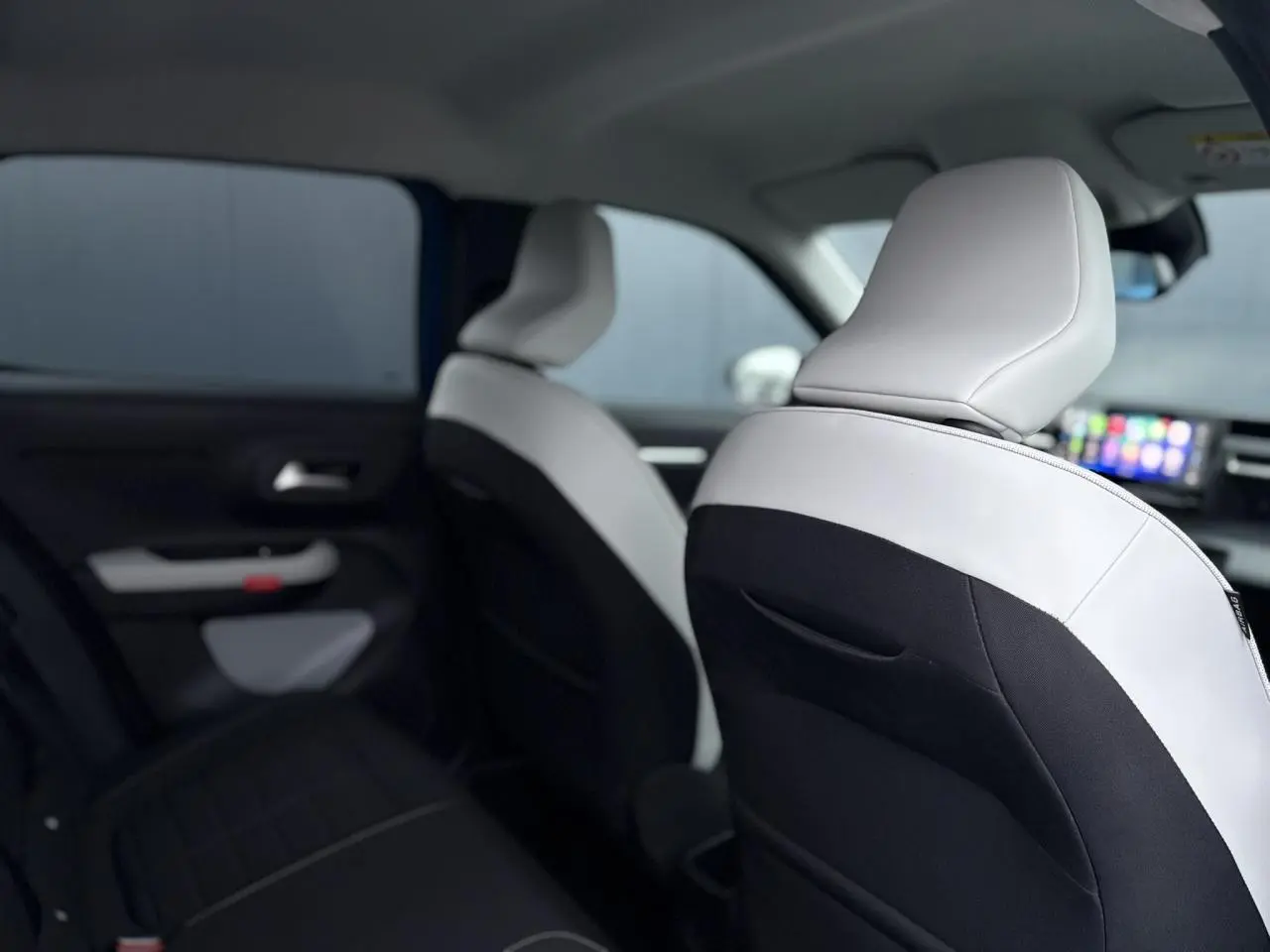Vue intérieure arrière droite de la Citroën C3 2025 avec sièges bicolores noir et blanc et écran tactile central visible.