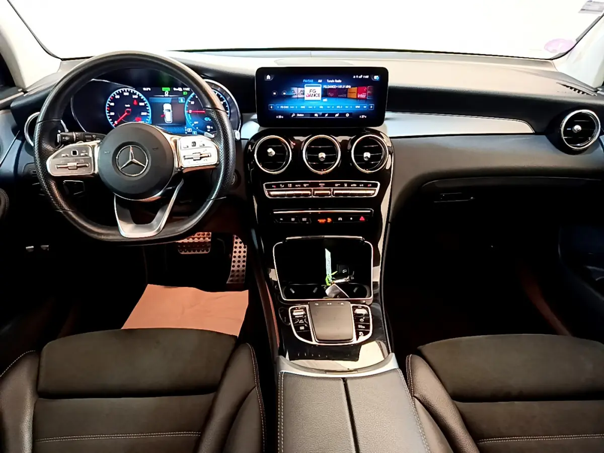 Vue intérieure avant du Mercedes GLC 300 E AMG Line 2021, tableau de bord noir avec écran tactile et volant multifonctions cuir.