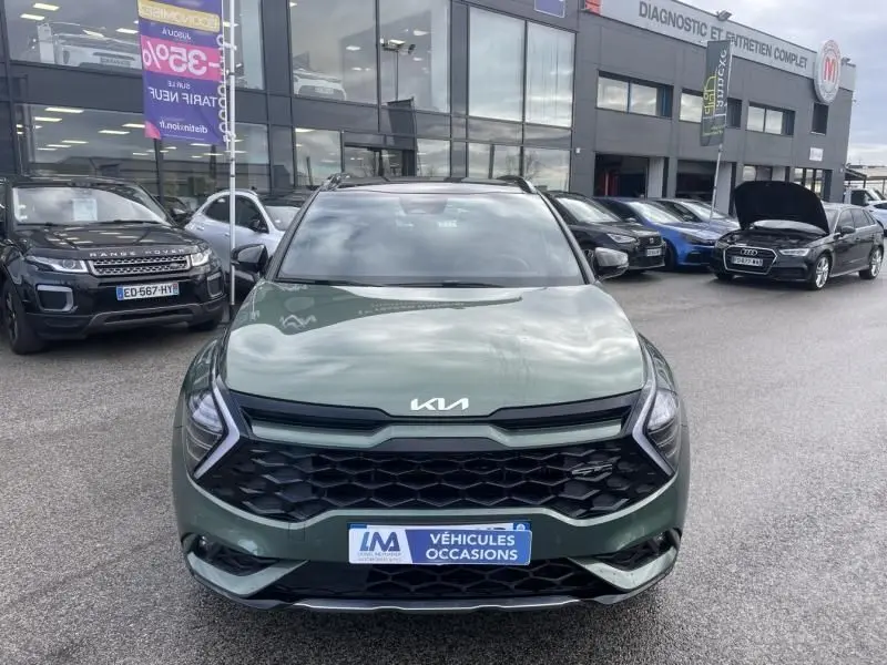 Vue de face d’un KIA SPORTAGE 2022 vert métal avec calandre noire et logo KIA sur parking de véhicules d’occasion.