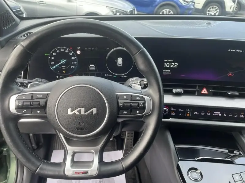 Vue intérieure centrée sur le volant KIA et le tableau de bord numérique du Sportage 2022, avec écran tactile et commandes intégrées.