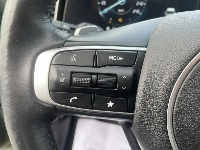 Gros plan sur les commandes gauche du volant noir du KIA Sportage 2022, boutons mode, volume et appel visibles.