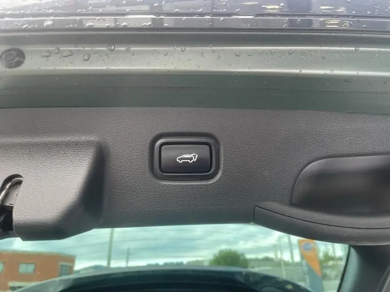 Bouton d'ouverture électrique du coffre sur le hayon intérieur d'un KIA SPORTAGE vert métal, vue rapprochée.