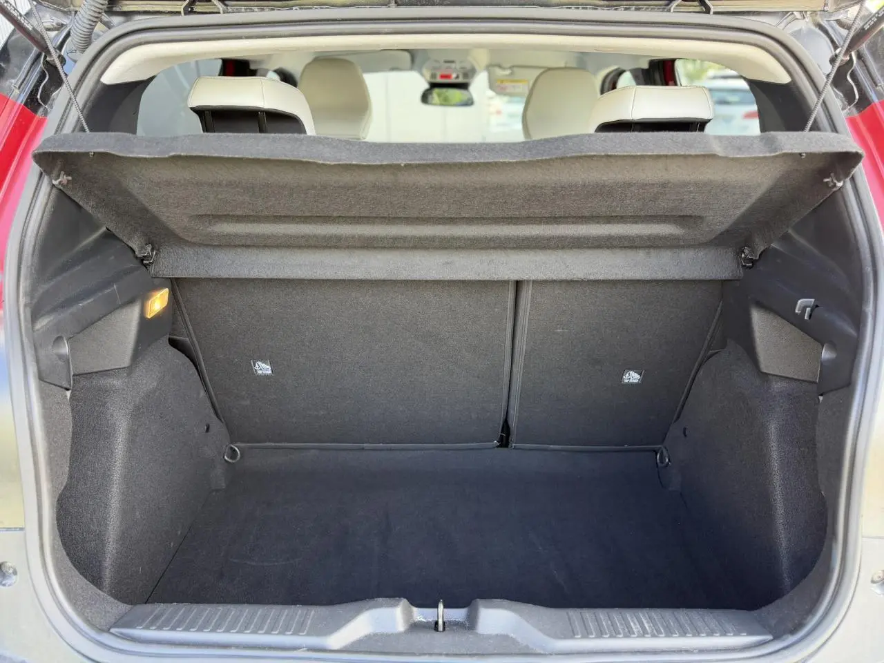 Vue intérieure du coffre ouvert d'une Citroën C3 Rouge Elixir, montrant l'espace de rangement et les sièges arrière beiges.