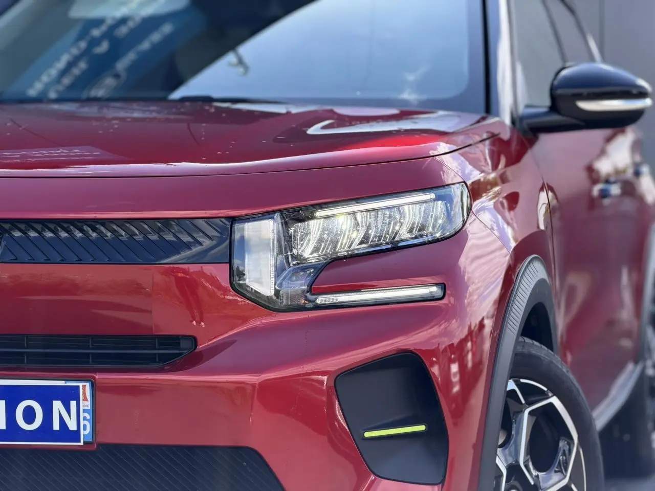 Gros plan sur le 3/4 avant droit de la Citroën C3 Rouge Elixir avec ses phares LED allumés et jantes alliage visibles.