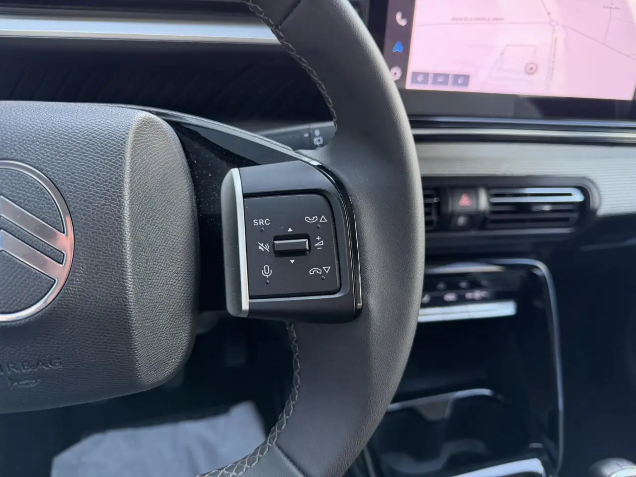 Gros plan sur la commande gauche du volant noir de la Citroën C3 2025, avec écran GPS visible en arrière-plan.
