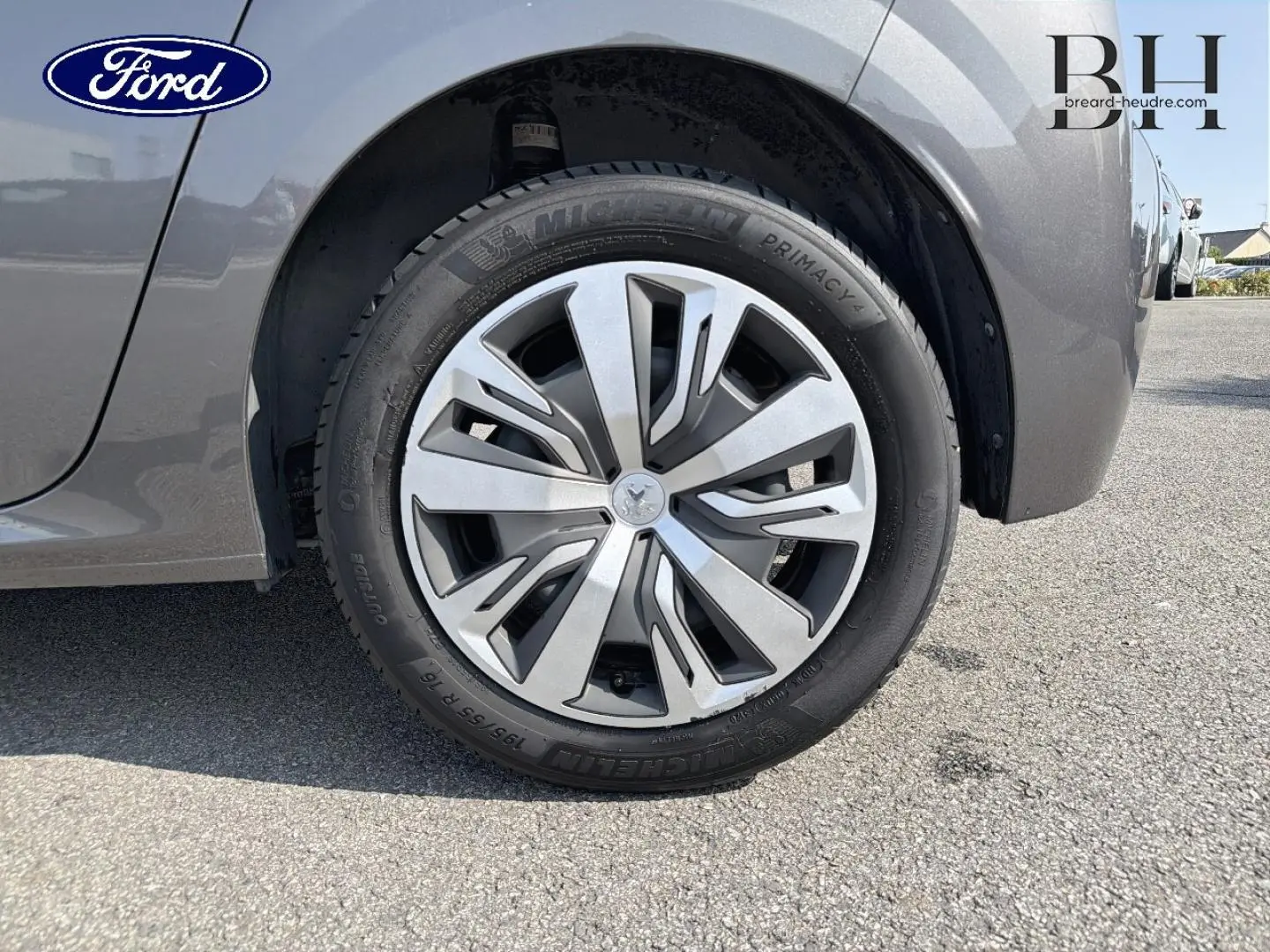 Gros plan sur la roue avant gauche d'une Peugeot 208 gris Platinium avec enjoliveur et logo lion central.