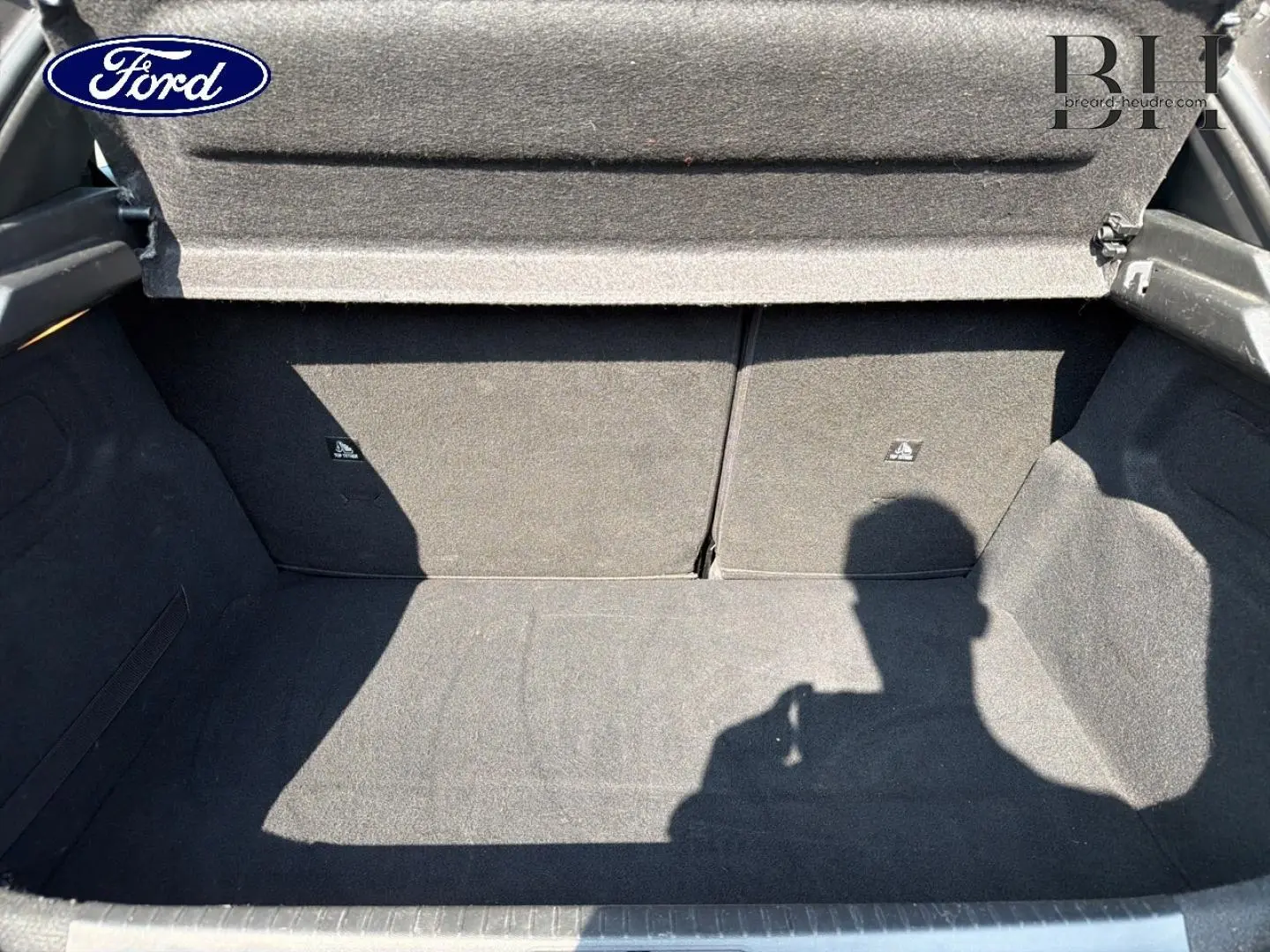 Coffre ouvert d’une Peugeot 208 gris Platinium, montrant l’espace de chargement intérieur vide et la tablette cache-bagages.