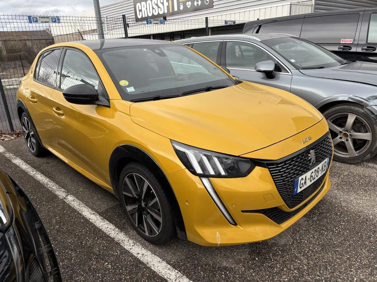 Peugeot 208 GT jaune vue 3/4 avant droit, avec calandre noire et feux LED en forme de griffes.