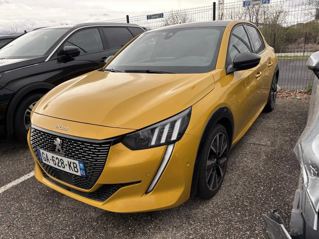 Peugeot 208 GT jaune vue 3/4 avant droit, avec calandre noire et feux LED distinctifs, stationnée en extérieur.