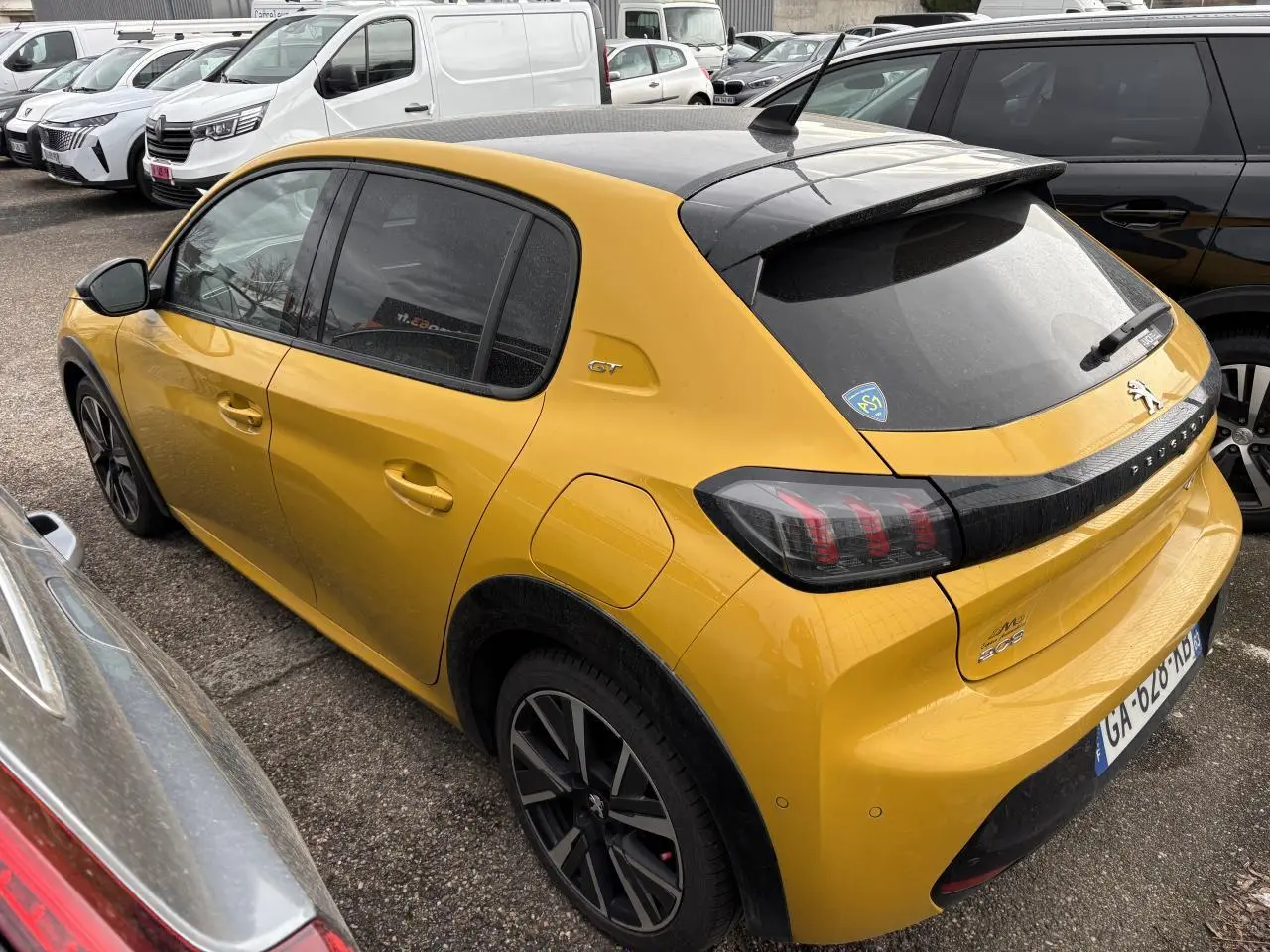 Peugeot 208 GT jaune vue 3/4 arrière droit, toit noir et feux arrière à griffes distinctifs.