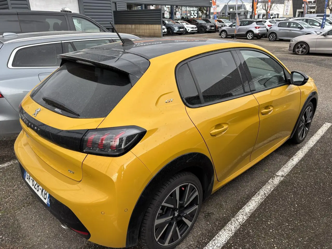 Peugeot 208 GT jaune vue 3/4 arrière droit, toit noir et jantes alliage distinctives, stationnée en extérieur.