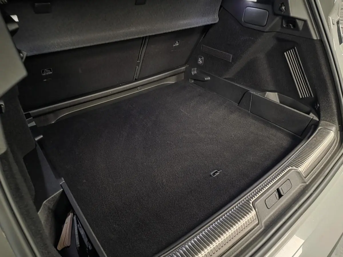 Coffre ouvert du DS7 Crossback gris, montrant le tapis de sol et les rangements latéraux noirs.
