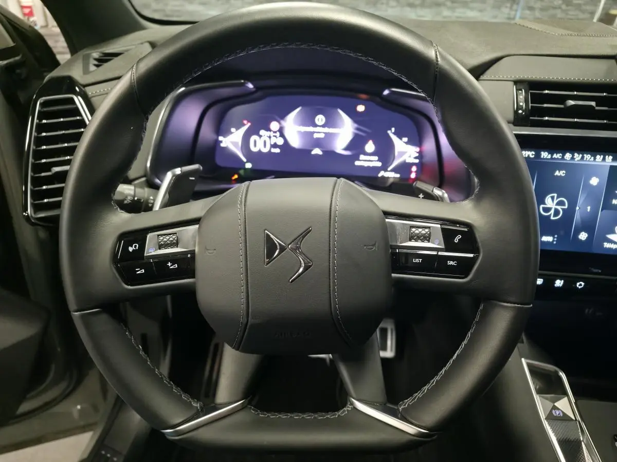 Vue rapprochée du volant en cuir noir du DS7 Crossback 2025 avec commandes intégrées et tableau de bord numérique lumineux.