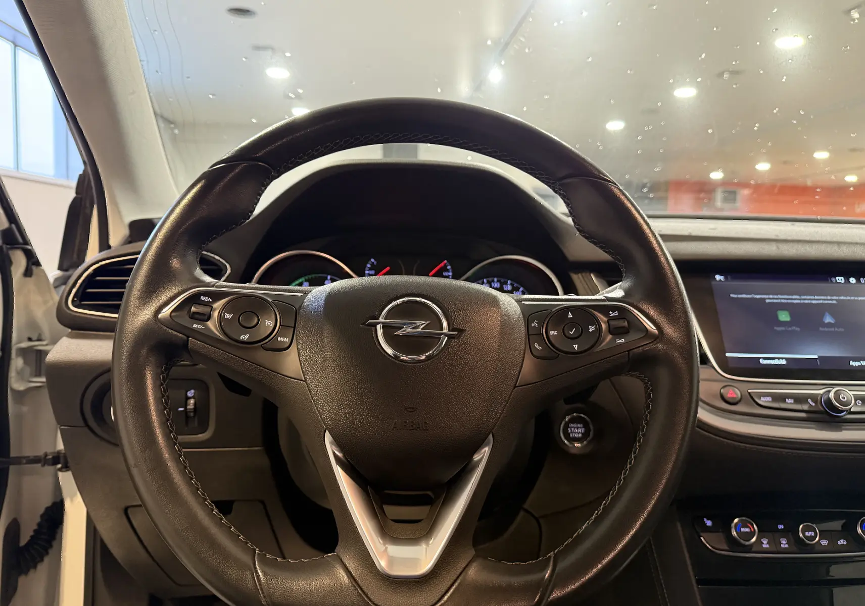 Vue centrée sur le volant en cuir noir d’un Opel Grandland X hybride blanc, avec tableau de bord et écran tactile visibles.