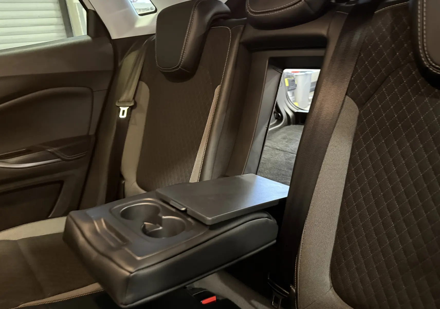 Vue intérieure arrière de l’Opel Grandland X 1.6 Hybrid Turbo 2021, sièges noirs avec accoudoir central et passe-trou vers le coffre.