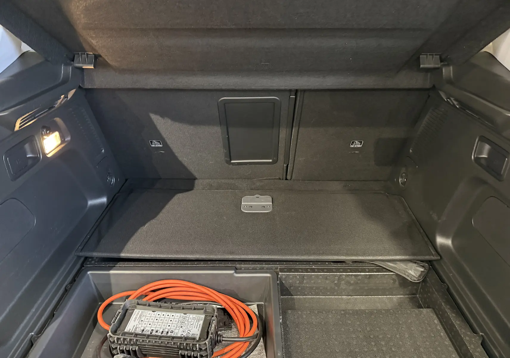 Vue du coffre ouvert de l’Opel Grandland X hybride blanc, montrant le compartiment de rangement avec câble de recharge.