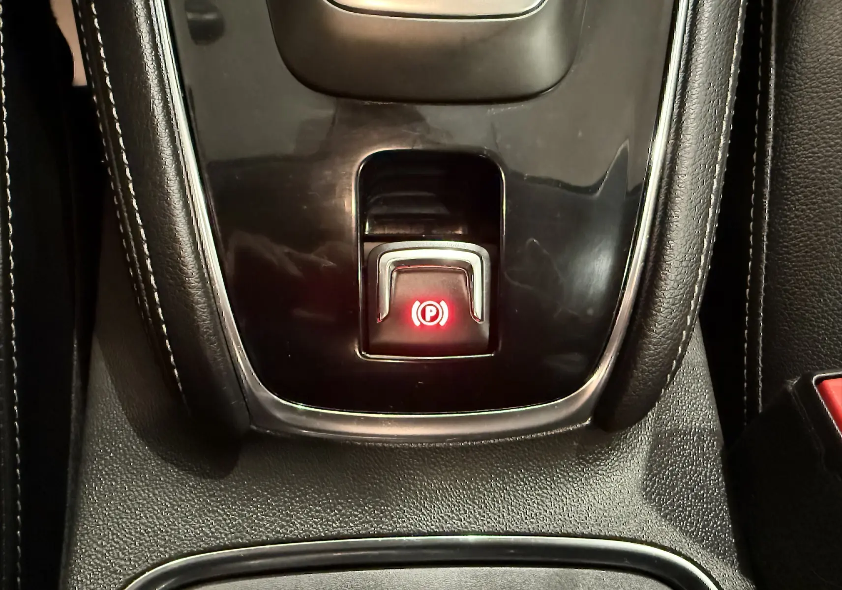 Gros plan sur le bouton de frein à main électronique rouge dans la console centrale de l’Opel Grandland X hybride rechargeable.