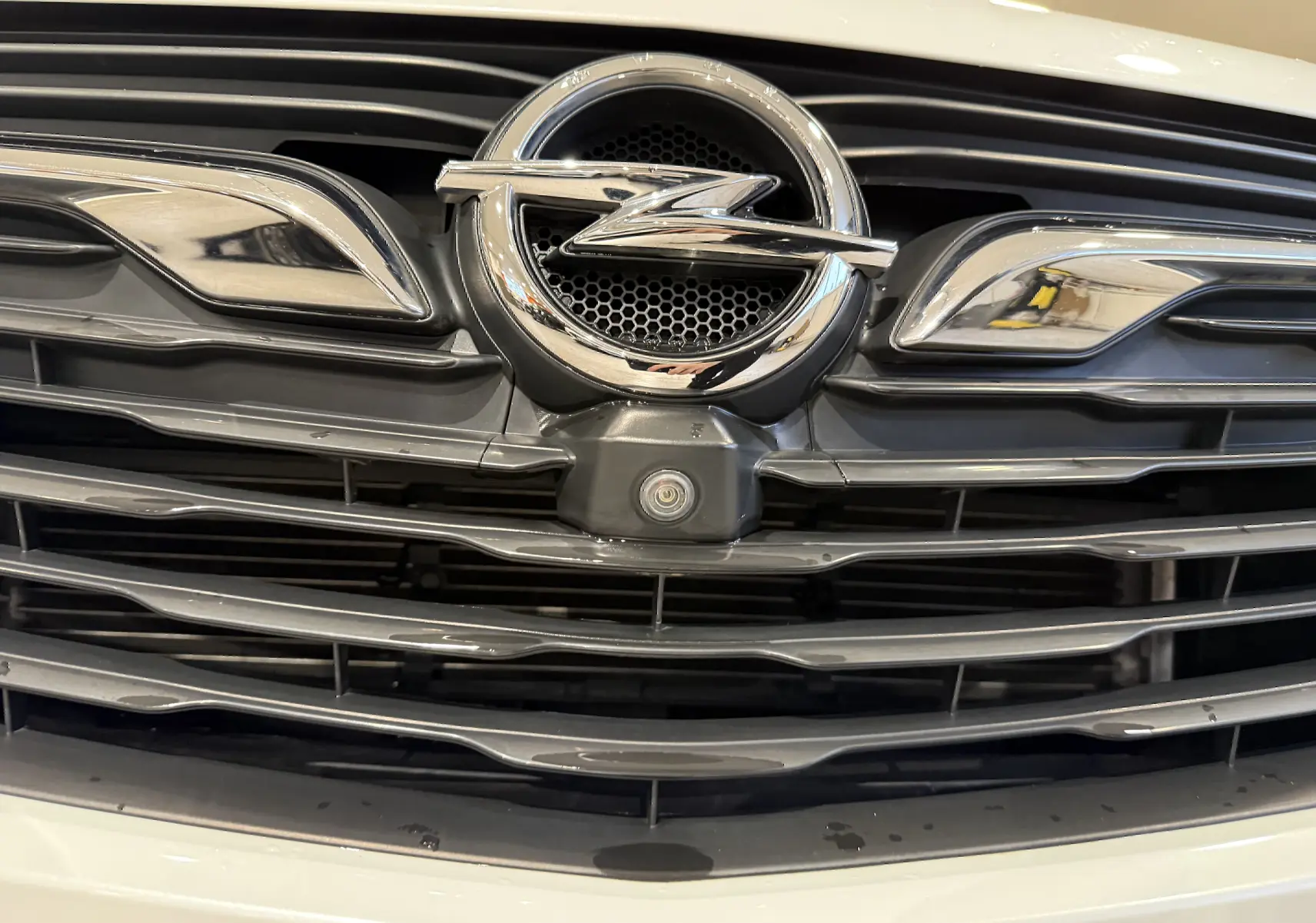 Gros plan sur la calandre avant blanche de l’Opel Grandland X avec logo chrome et caméra intégrée.