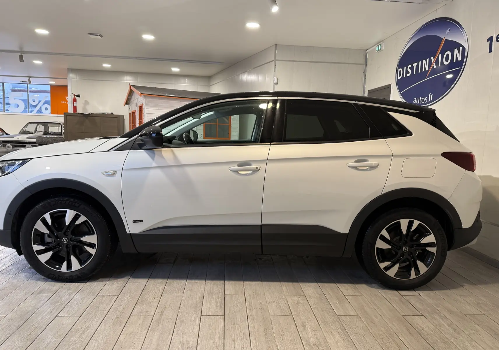 Vue de profil côté gauche d’un Opel Grandland X blanc avec toit noir et jantes alliage bicolores, en intérieur showroom.